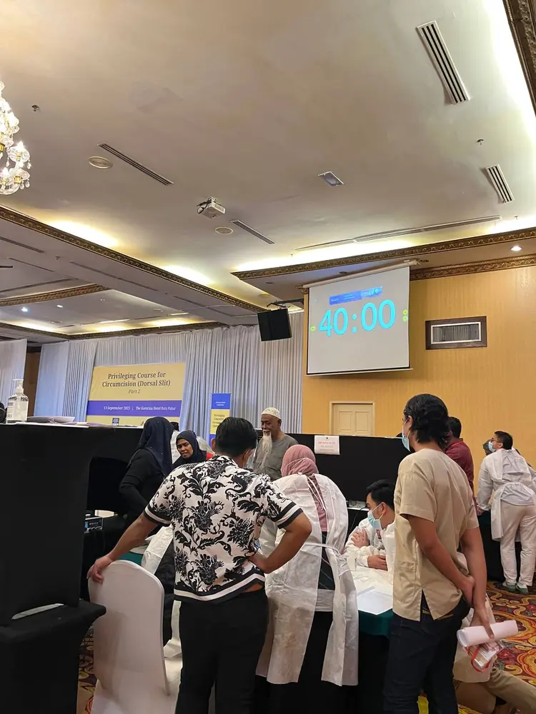 Suasana dewan kursus PCC2-1 di The Katerina Hotel — peserta berbaju pelindung bersedia di stesen penilaian, sepanduk kursus dan pemasa 40 minit pada skrin