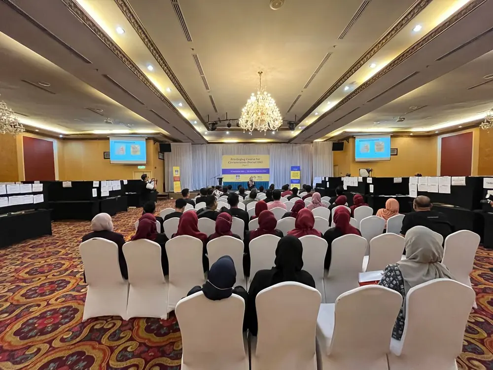 Pandangan keseluruhan dewan kursus PCC2-1 — pentas, sepanduk kursus dan peserta duduk mengikut baris
