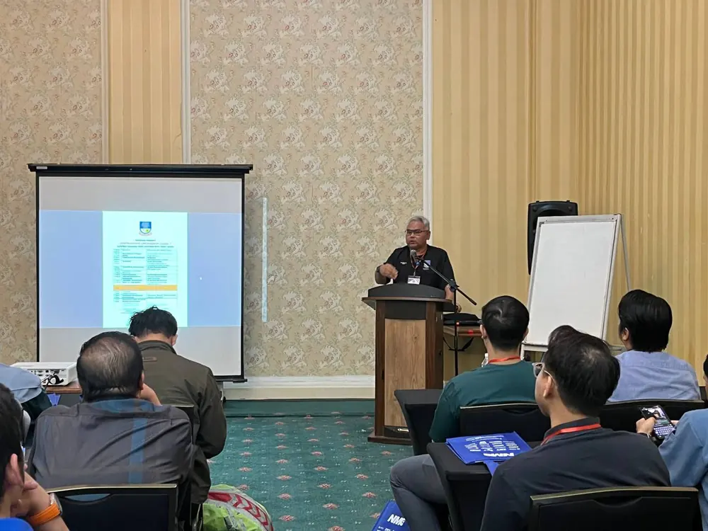 Penceramah menyampaikan taklimat program PCC2-1 di podium, dengan jadual kursus dipaparkan pada skrin